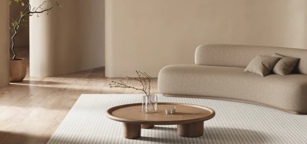 Salón minimalista en tonos beige con sofá curvo y mesa de madera natural